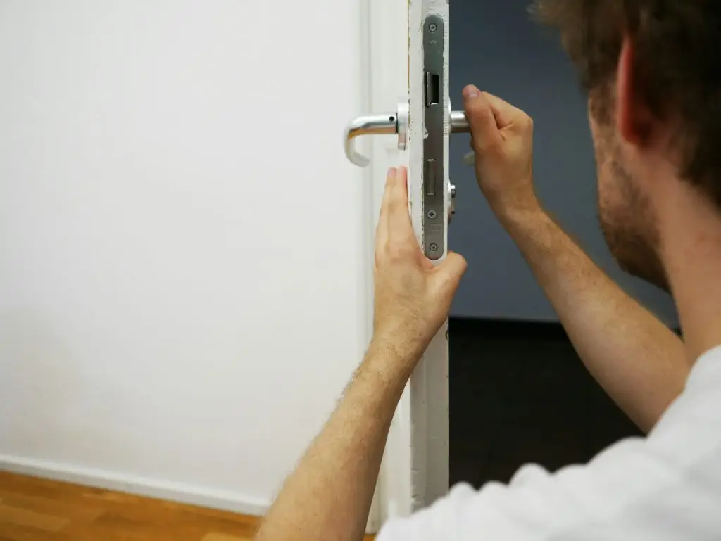 A man in a white shirt attempting to fix a door lock